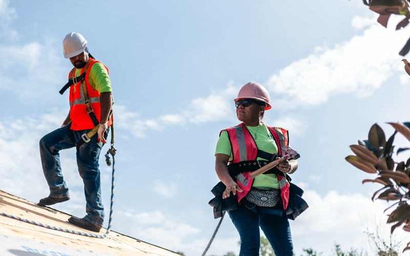 female and male roofer in safety equipment standing on a roof deck