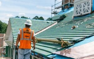 green tile roof mid-installation with man in Baker safty equipment inspecting work