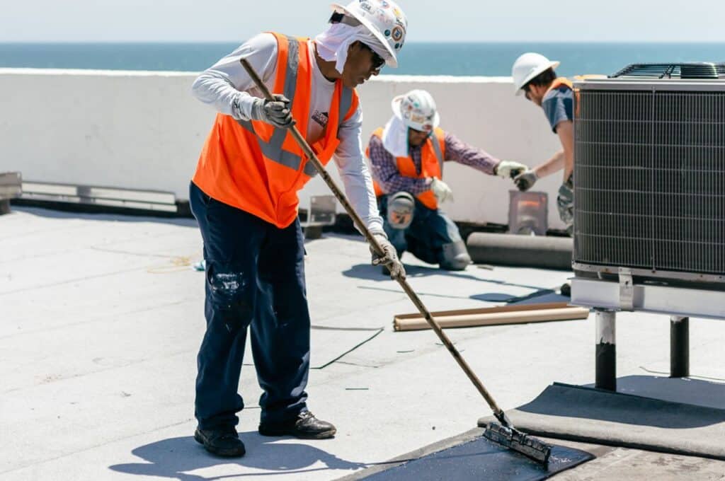 baker roofing employee laying a modified bitumen roof with two men working behind him and overlooking the ocean