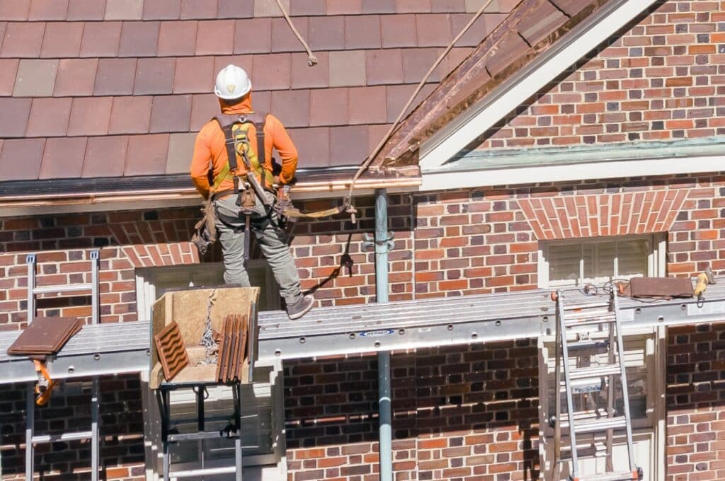 man in safety working on copper gutters with ladder
