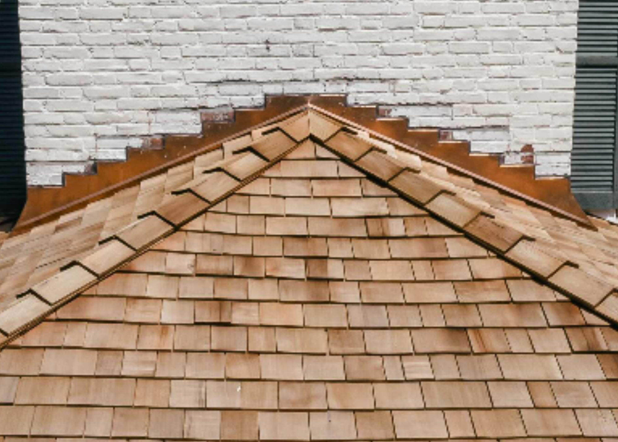 close up of cedar roof with copper flashing against white brick home