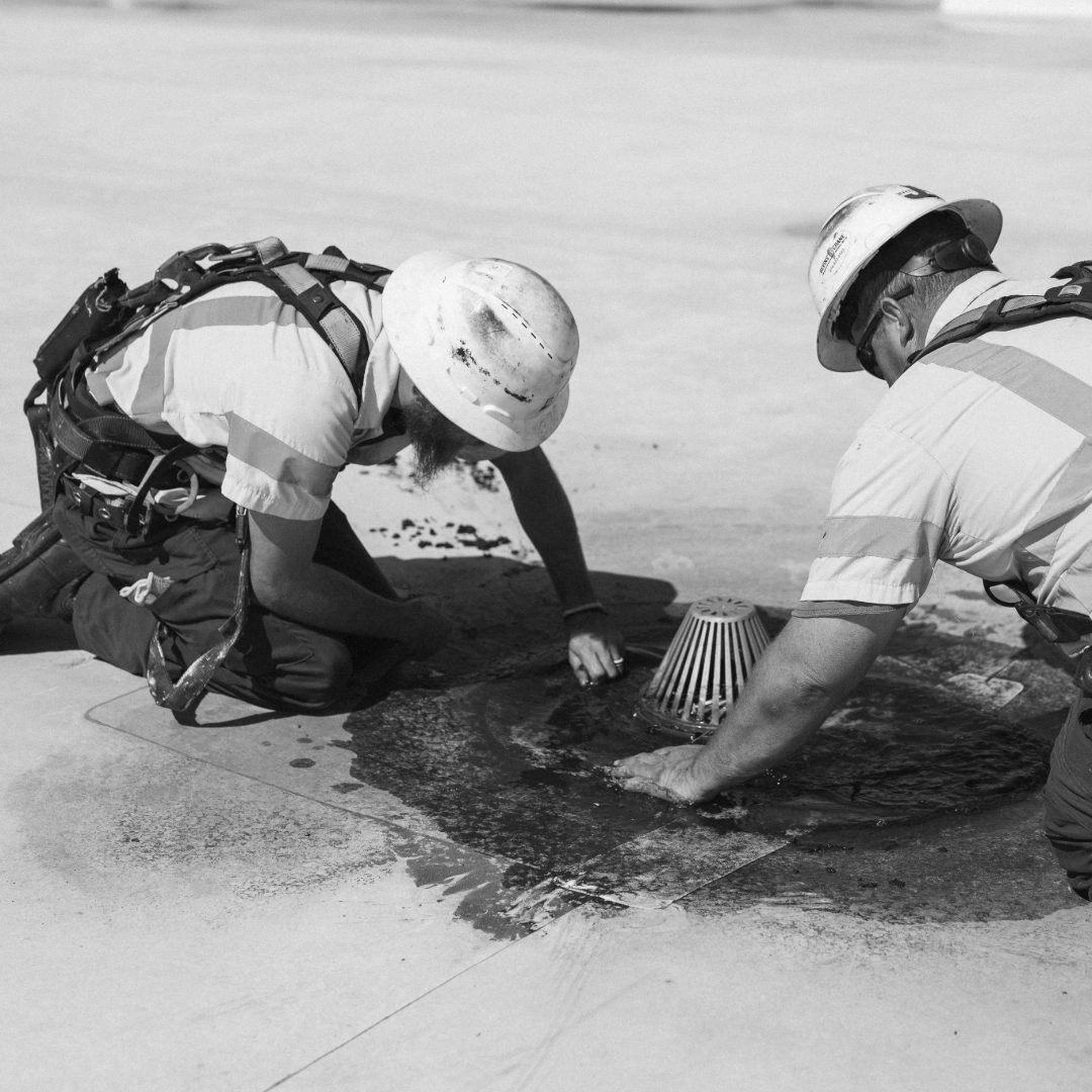 two roofers working on clearing a roof drain in uniform