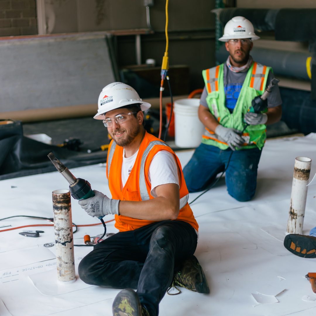 two roofers in training posing for a photo on a mock up roof