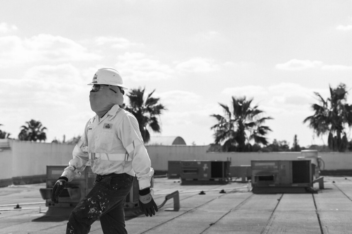 black and white man in uniform working roof palm trees in back